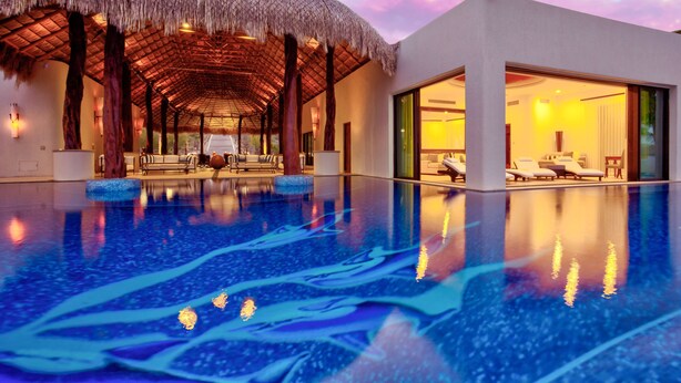 Ein modernes Resort mit einem großen Infinity-Pool, einem strohgedeckten Gebäude und einem gut beleuchteten Innenbereich.