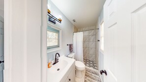 Une salle de bain avec un lavabo, des toilettes et une douche, le tout de couleur blanche.