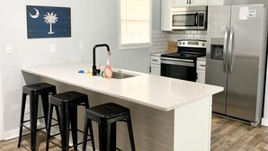 Una cocina moderna con una isla central, taburetes negros, electrodomésticos de acero inoxidable y un elemento decorativo en la pared.