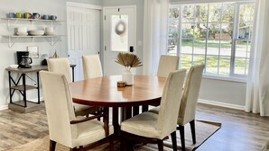 Un comedor con una mesa redonda de madera, seis sillas, un ventilador de techo y vistas al exterior a través de amplios ventanales.