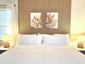 Ein Hotelzimmer mit einem Bett, zwei Kissen, einem Kopfteil aus vertikalen Holzleisten, zwei floralen Bildern an der Wand und Nachttischlampen.
