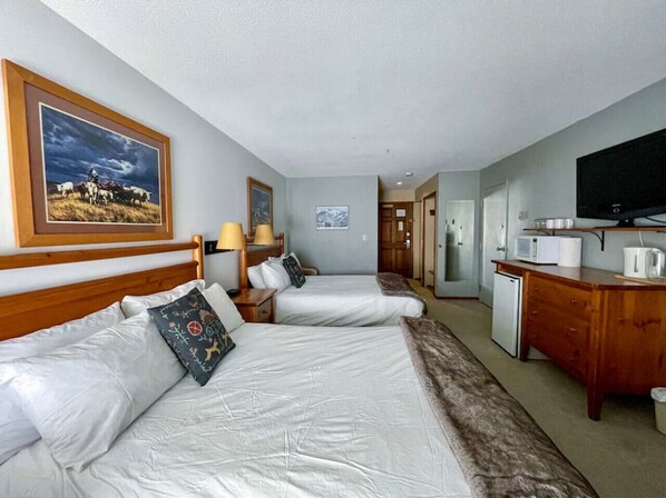 A hotel room with two beds, a wooden headboard, a television, a microwave, and a small kitchenette. - Apex Mountain ~ Hillside Hideout ~ Apex Mountain Inn (Apex Mountain Resort)