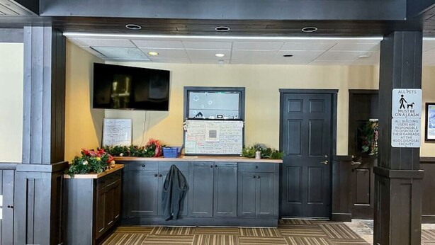 A reception area with a counter, a wall-mounted TV, and a sign indicating pet policy. - Apex Mountain ~ Hillside Hideout ~ Apex Mountain Inn (Apex Mountain Resort)