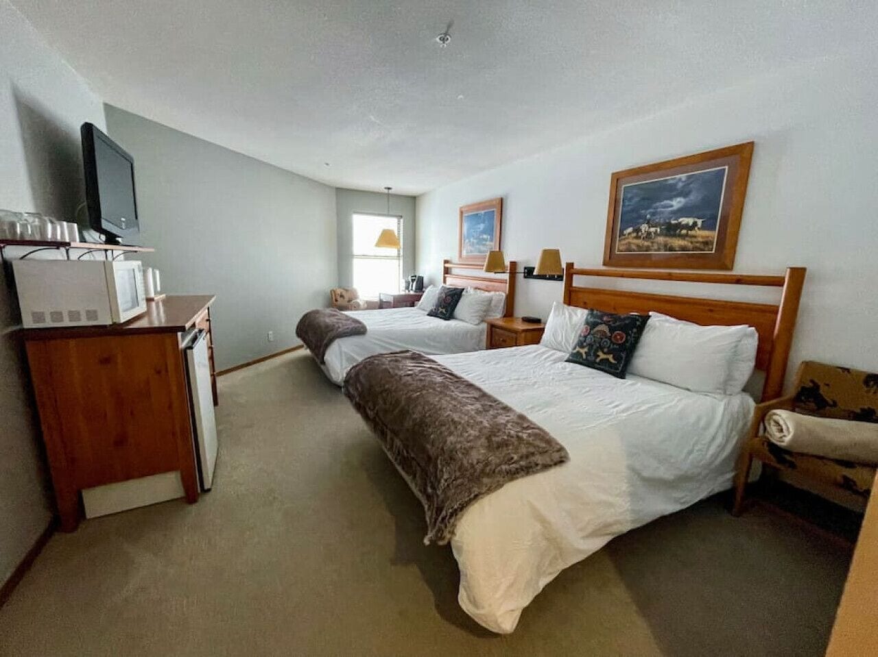 A hotel room with two beds, a desk with a computer, a lamp, and a painting on the wall.