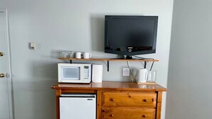 A compact kitchenette with a microwave, toaster, and coffee maker on a wooden countertop, a small refrigerator, and a television mounted on the wall. - Apex Mountain ~ Hillside Hideout ~ Apex Mountain Inn (Apex Mountain Resort)