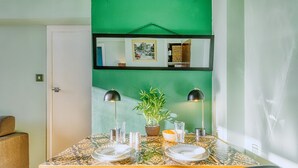 A dining table set with plates, cutlery, and glasses, flanked by chairs, with a potted plant and a framed picture above. - Hardwood Home  - One Bedroom Apartment, Sleeps 2 (London)