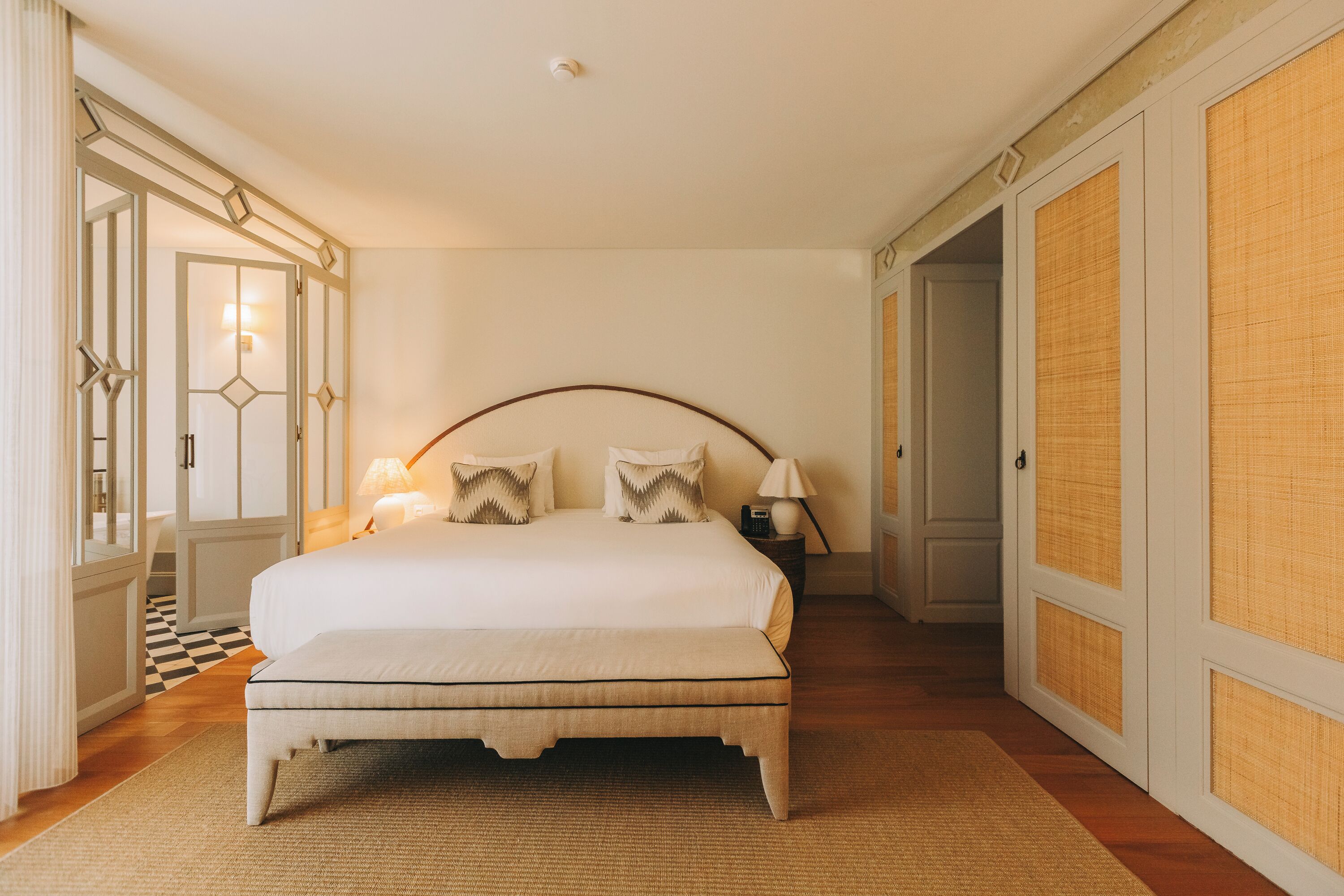 A spacious bedroom with a large bed, a bedside table with lamps, and a checkered floor.