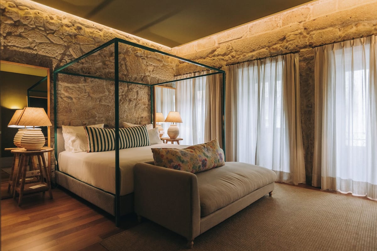 A four-poster bed with a stone wall backdrop, a sofa, and a nightstand with lamps.