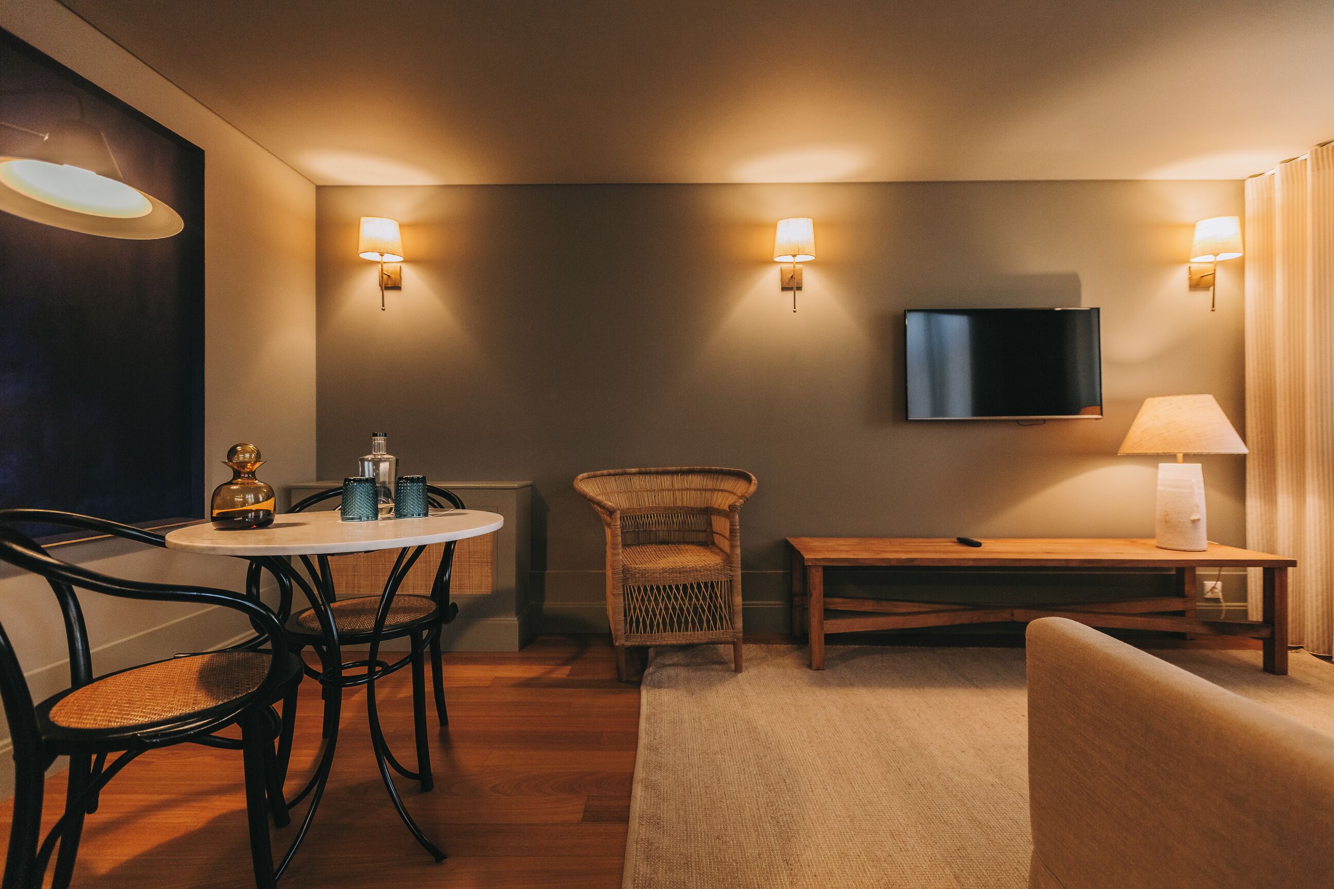 Habitación de hotel con comedor, televisor montado en la pared y lámpara en la mesita de noche.