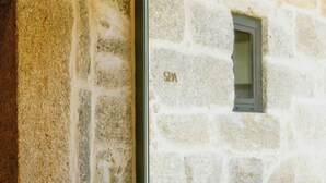 A cozy seating area with a cushioned bench against a stone wall, a window with the text "SPA" visible, and a wooden floor. - Torel Saboaria (Porto)