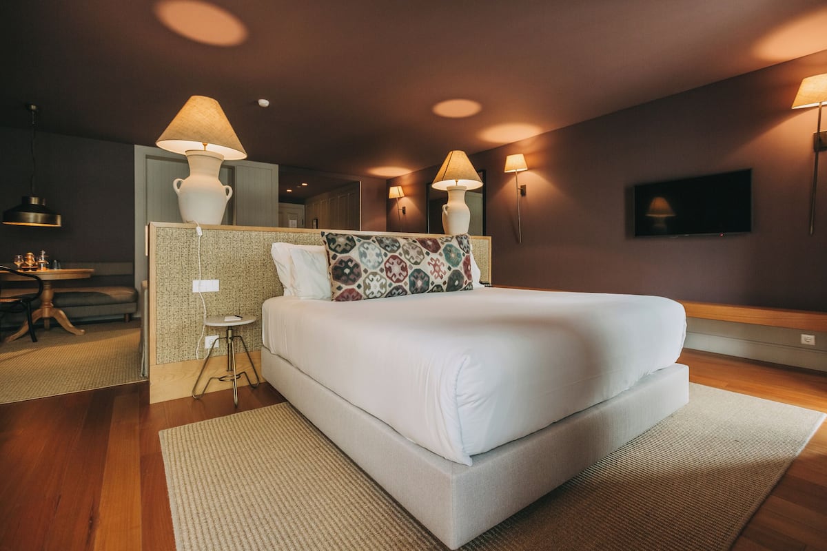 A modern hotel room with a large bed, bedside lamps, a small table, and a TV.