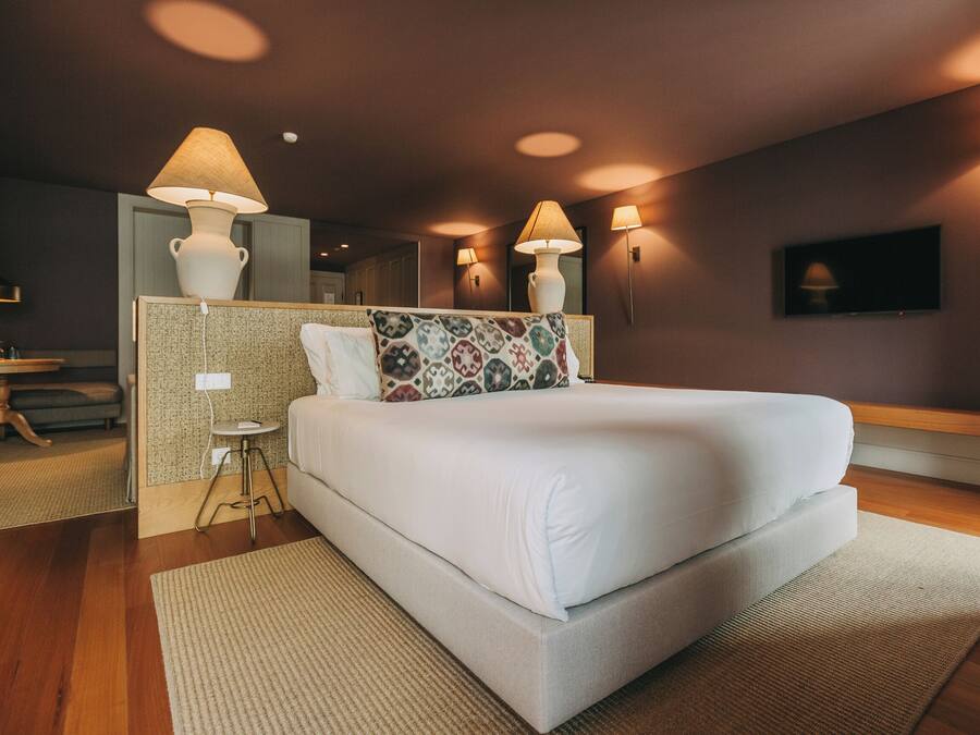 A modern hotel room with a large bed, bedside lamps, a small table, and a TV.