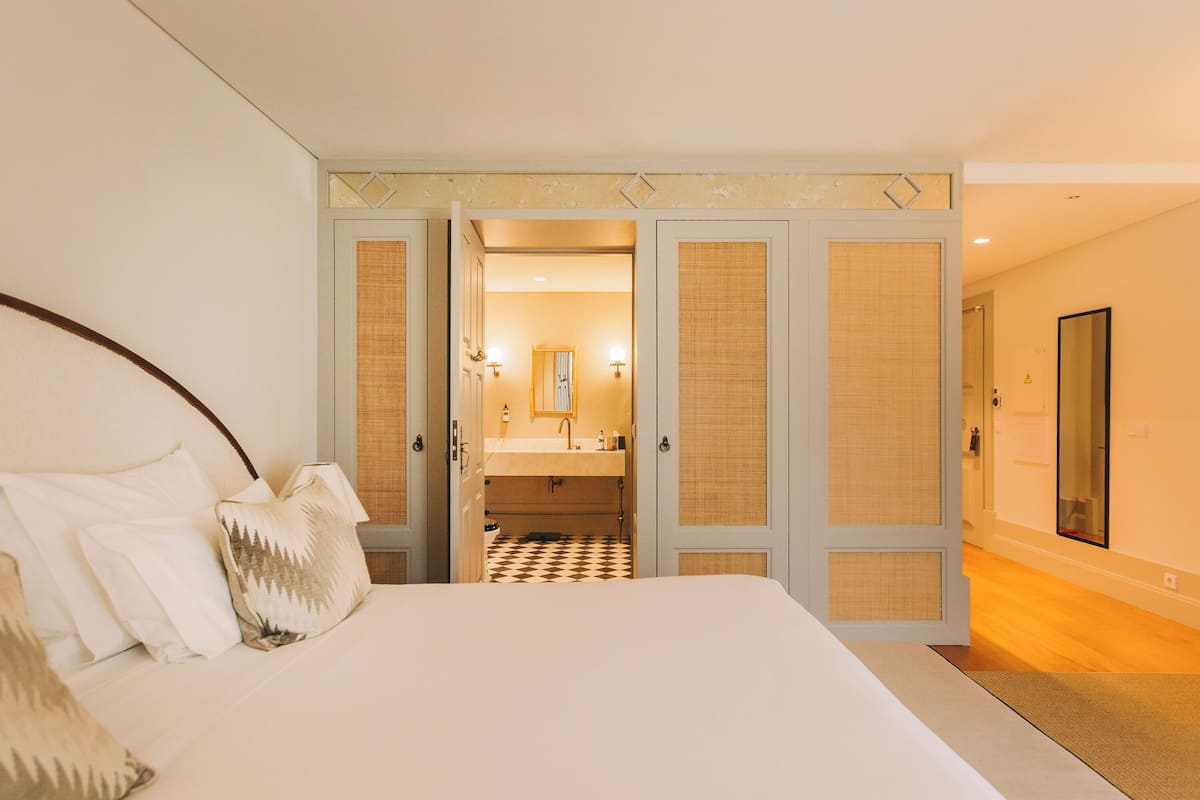 A bedroom with a large bed, a bathroom with a checkered floor, and a mirror on the wall.