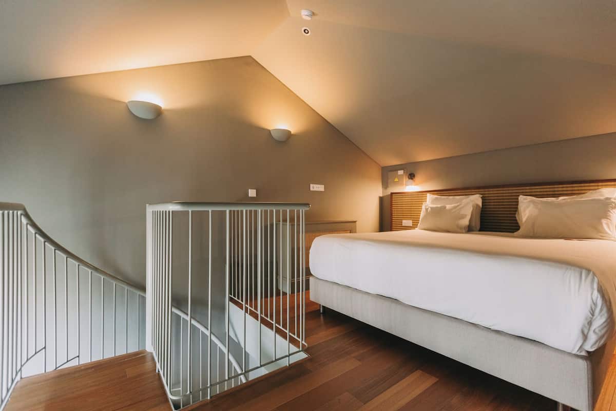 A bedroom with a bed, a staircase, and a wall-mounted light fixture.