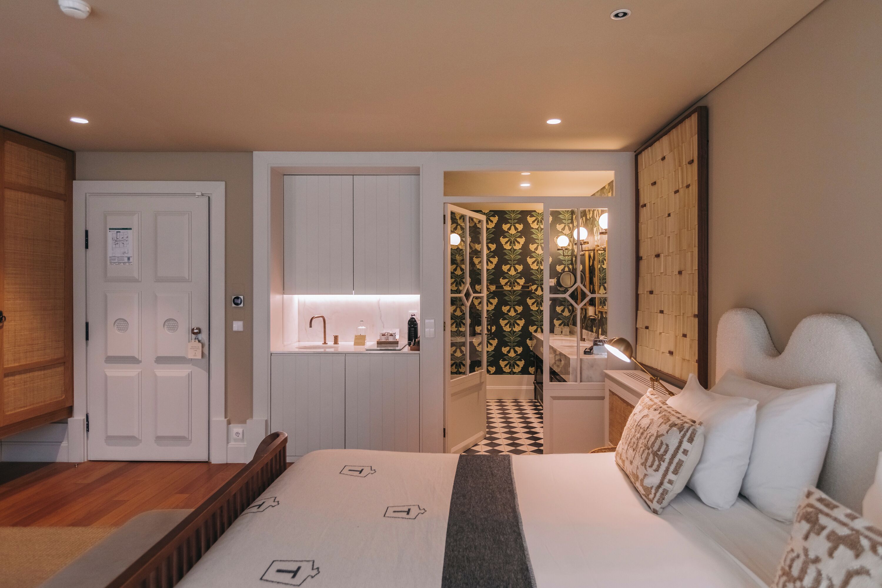 A hotel room with a bed, a bathroom with a mirror, and a kitchenette.