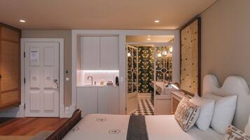 A hotel room with a bed, a bathroom with a mirror, and a kitchenette.