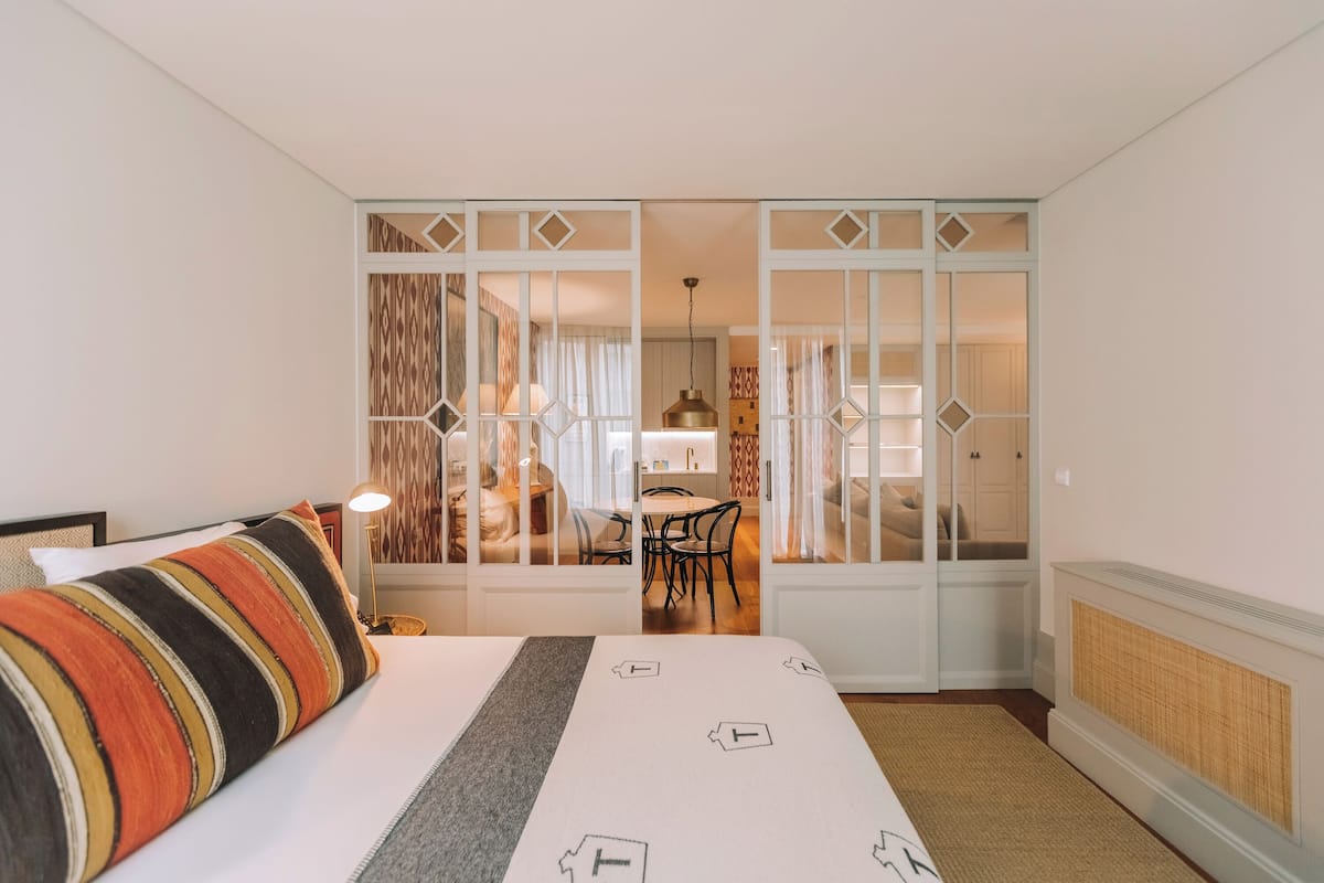 A hotel room with a bed, a desk, and a dining area visible through a partition.