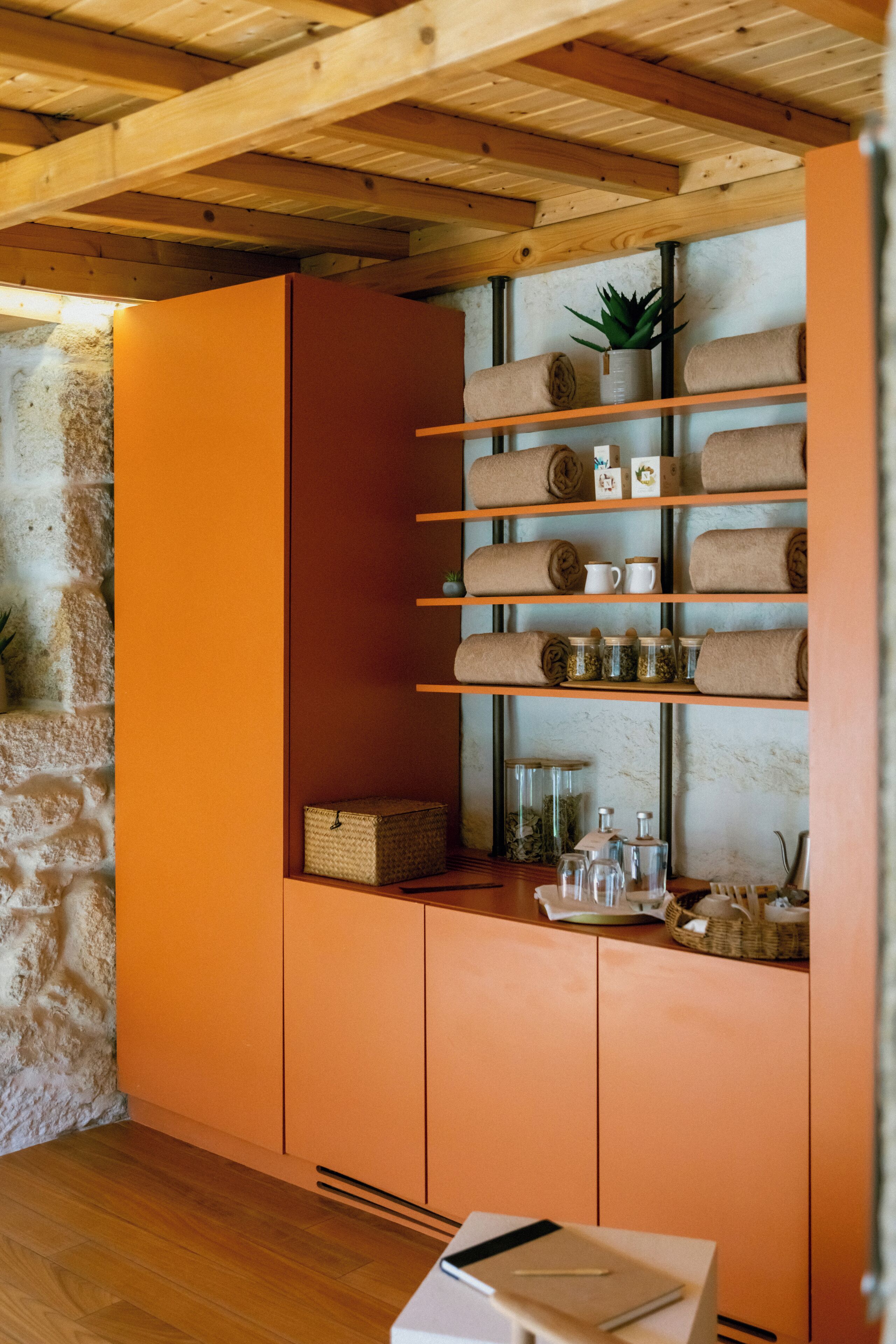 Una habitación con techo de madera, paredes anaranjadas y estantes con toallas y frascos.