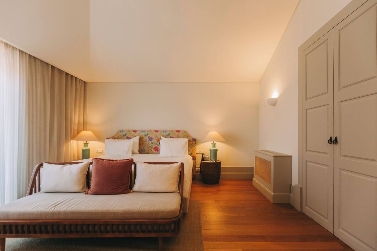 A hotel room with a bed, two bedside lamps, a nightstand, a wardrobe, and a window with curtains.