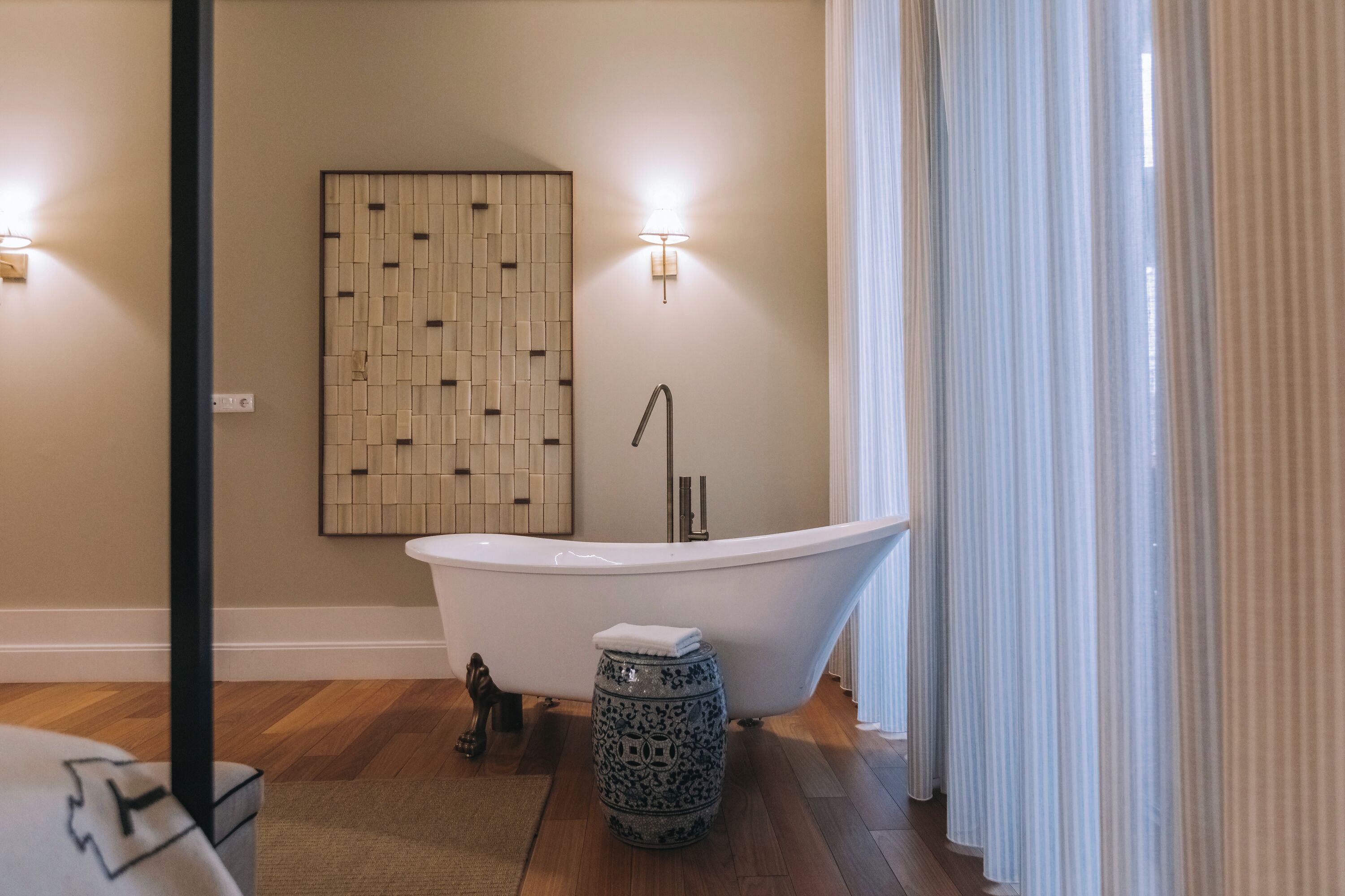 A modern bathroom with a freestanding bathtub, a decorative wall panel, and a small round table with a towel.