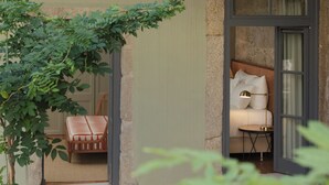 A room with a bed, a small table, and a chair. There is a window with curtains, and a plant is visible outside. - Torel Saboaria (Porto)