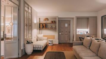 A modern living room with a sofa, a bed, a dining area, and a kitchen visible through an open door.