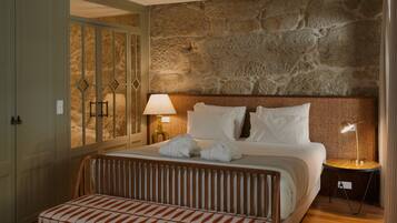 Una habitación de hotel con una cama grande, un banco de madera, una pared de piedra y una mesita de noche con lámpara.