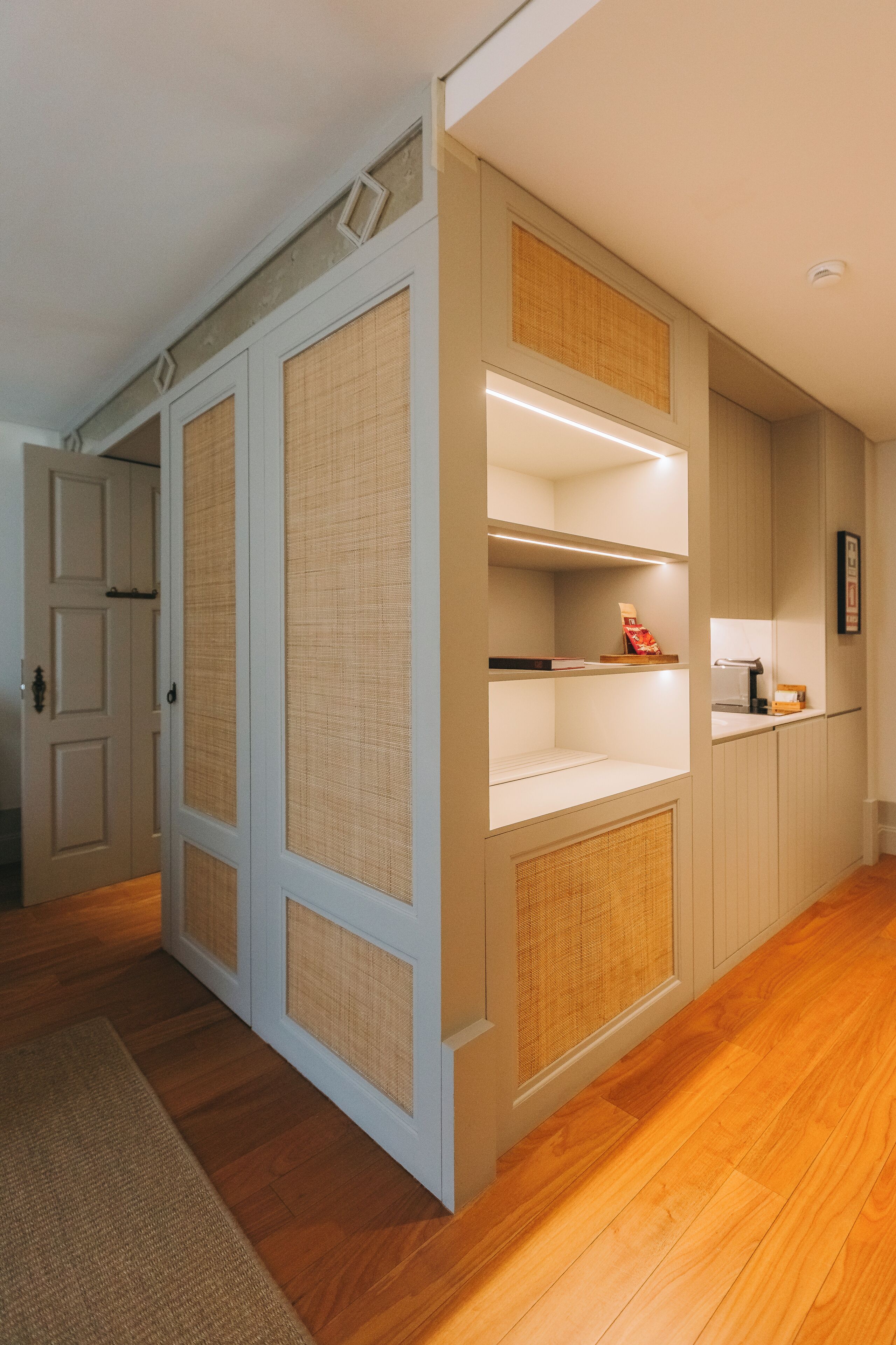 A hallway with wooden flooring, a door, and a wall with built-in shelving and a small table.