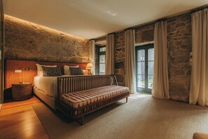 A bedroom with a stone wall, a bed, a bench, and a large window with curtains. - Torel Saboaria (Porto)