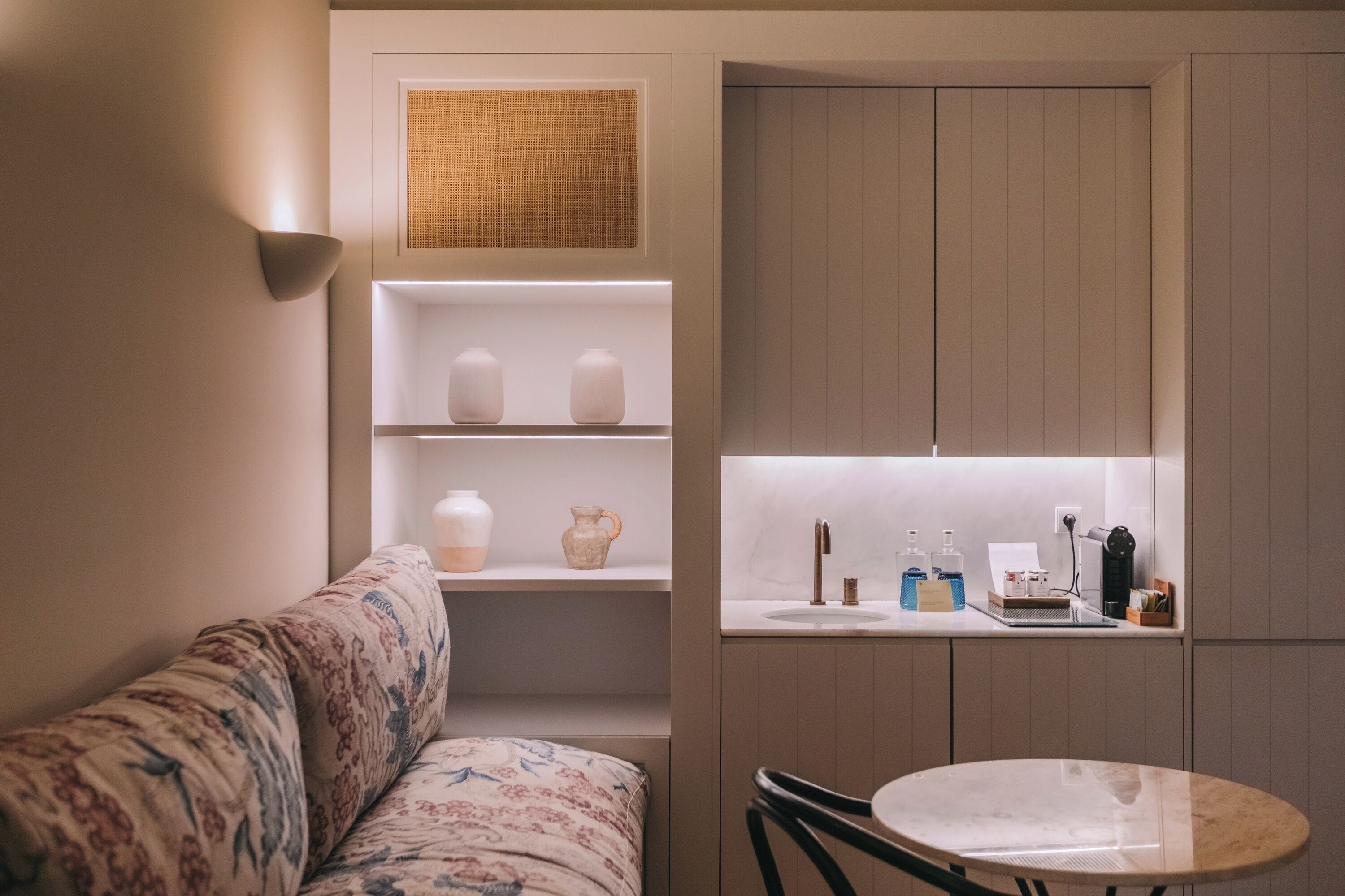 Un espacio habitable compacto con sofá, una mesa redonda, una zona de cocina con fregadero y estantes decorados con objetos.