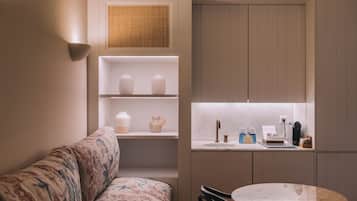 Un espacio habitable compacto con sofá, una mesa redonda, una zona de cocina con fregadero y estantes decorados con objetos.