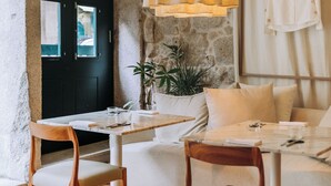 A modern living room with a stone wall, a black door, a white sofa, a wooden dining table, and a yellow pendant light. - Torel Saboaria (Porto)