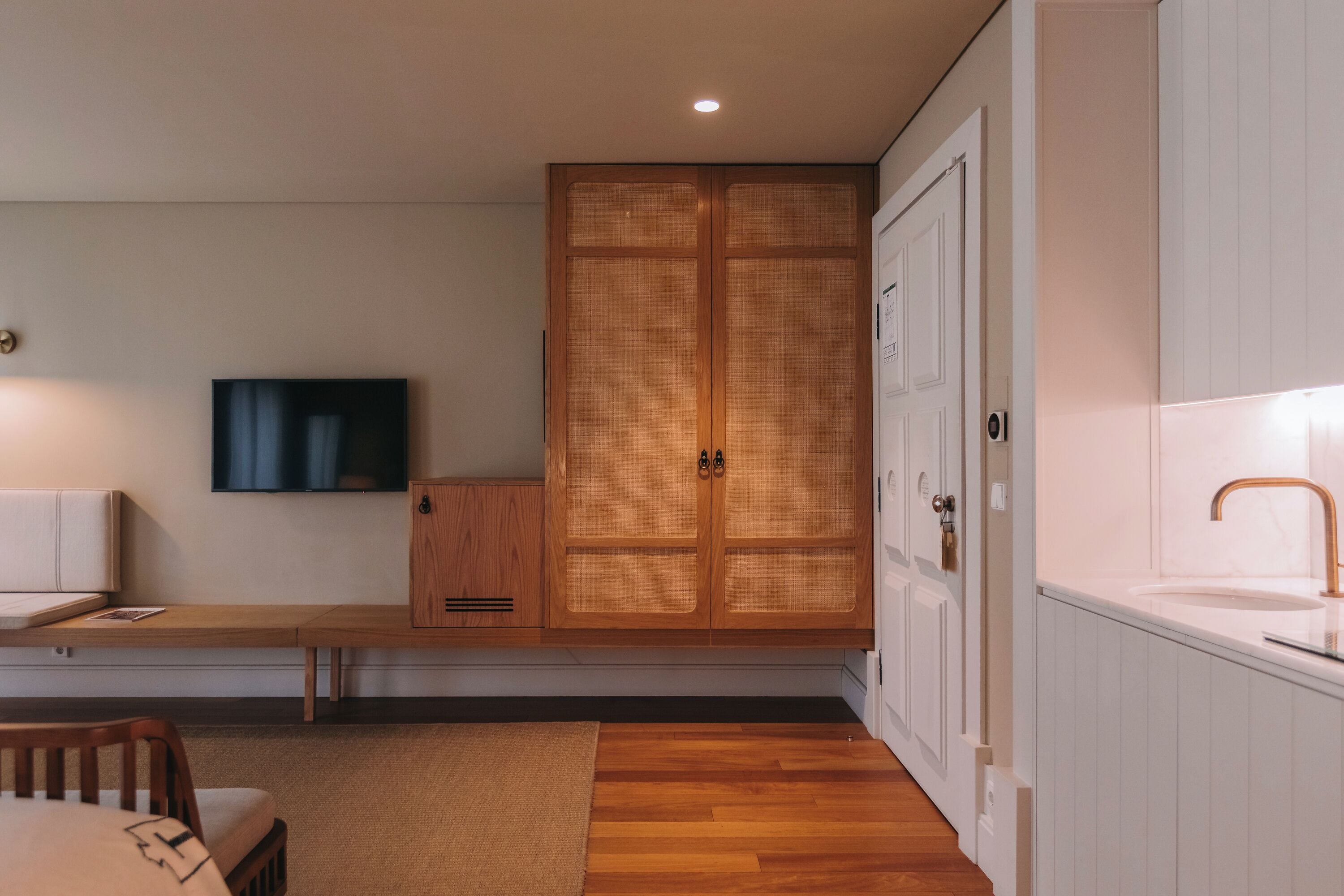 A modern room with a wooden wardrobe, a television, a bench, and a sink.