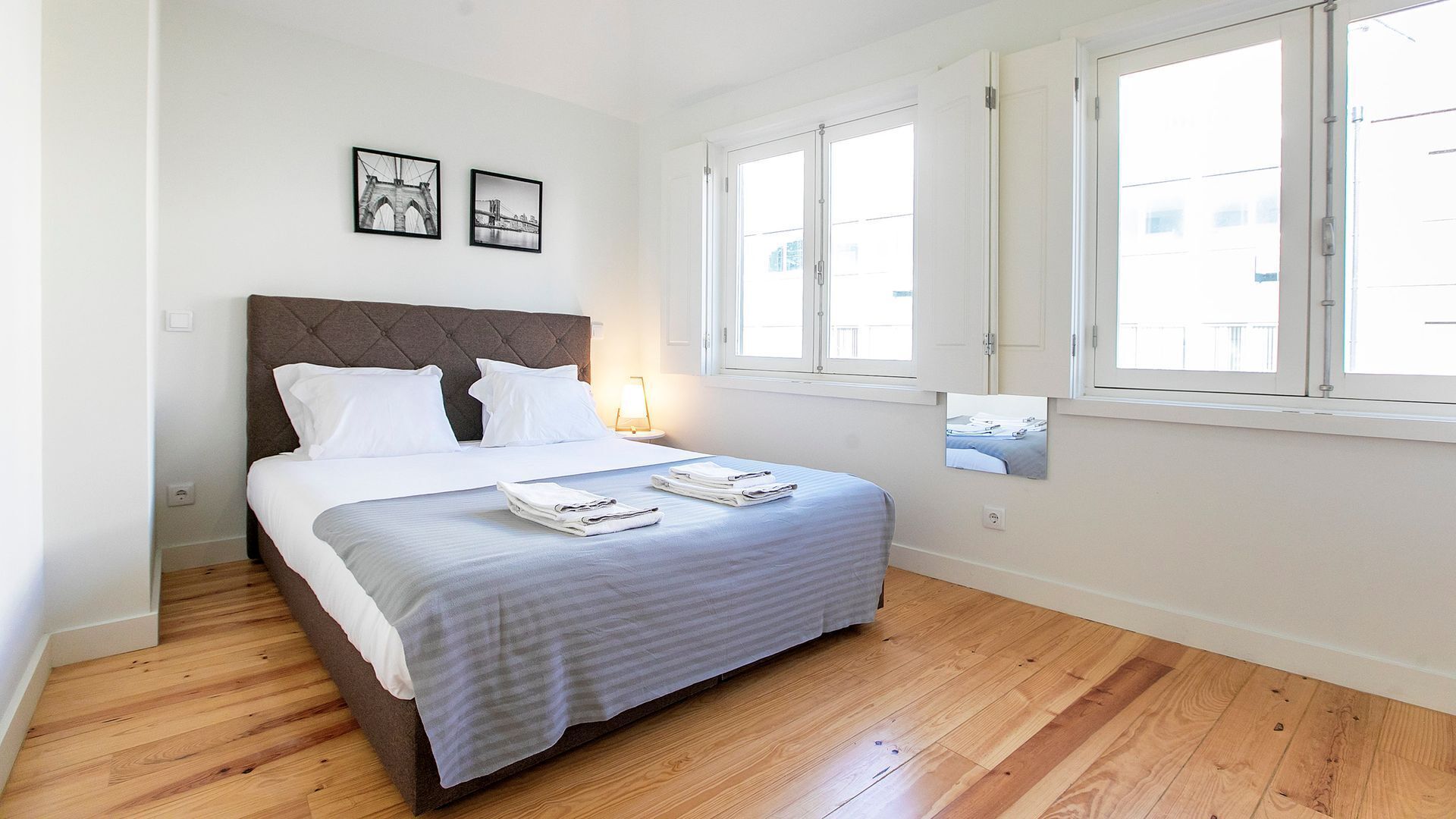 A neatly arranged bedroom with a bed, two bedside lamps, and a window with blinds.