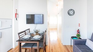 A modern kitchen with a flat-screen TV, wooden dining table with chairs, and a small seating area with a sofa and a side table. - Apartamento de 1 quarto em Santa Catarina (Porto)