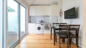 A compact kitchen with a washing machine, oven, and dining area with wooden chairs and a table. - Apartamento de 1 quarto em Santa Catarina (Porto)