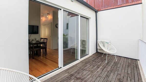 A balcony with a wooden deck, a dining area with a table and chairs, and a white chair.