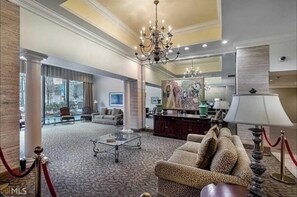 Experience the grandeur of our lobby, featuring a stunning chandelier, a beautiful painting, and a cozy seating area with a patterned sofa and armchairs.