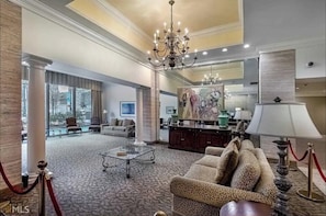 Experience the grandeur of our lobby, featuring a stunning chandelier, a beautiful painting, and a cozy seating area with a patterned sofa and armchairs.