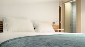 A bedroom with a bed, two pillows, a bedside table, and a door leading to a bathroom.