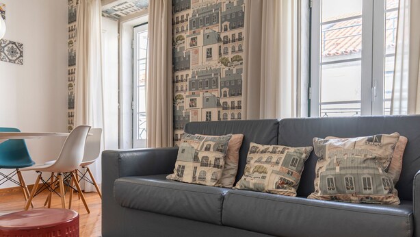A living room with a grey sofa, two patterned cushions, a red stool, and a blue chair.