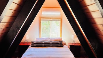 A bedroom with a sloped ceiling, a bed, a window, and a hanging light fixture.
