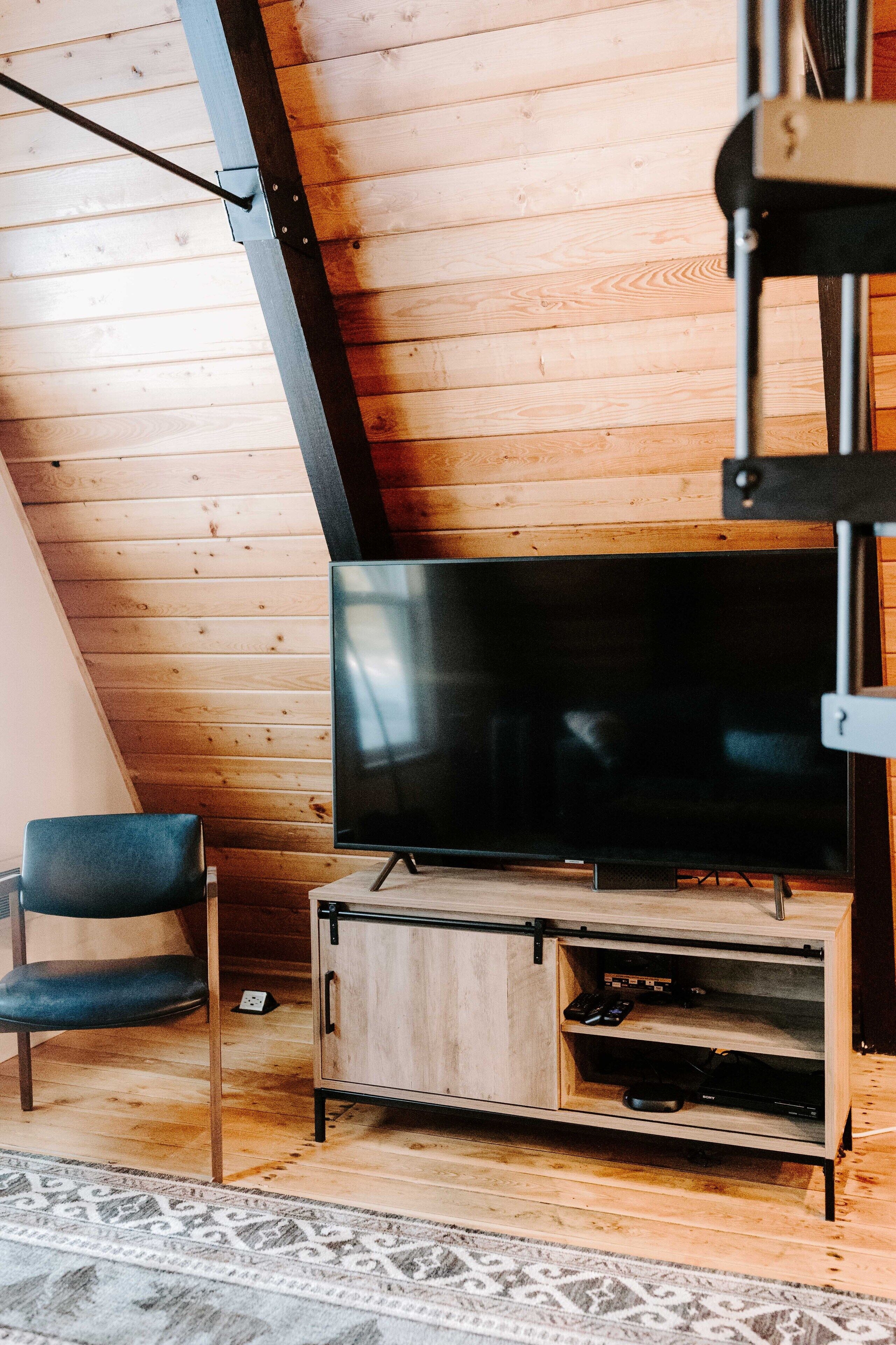 Een moderne woonkamer met een houten vloer, een flatscreen televisie op een houten dressoir, een blauwe fauteuil en een vloerkleed met een patroon.