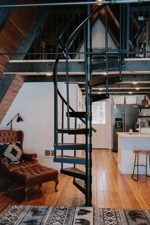 Een modern loft met een zwarte spiraaltrap, houten vloeren, een gezellige leren fauteuil en een keuken op de achtergrond.