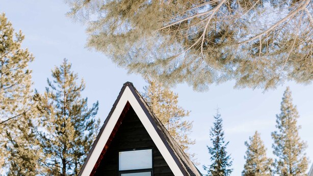 Une cabane avec un toit triangulaire, une porte blanche et de grandes fenêtres.