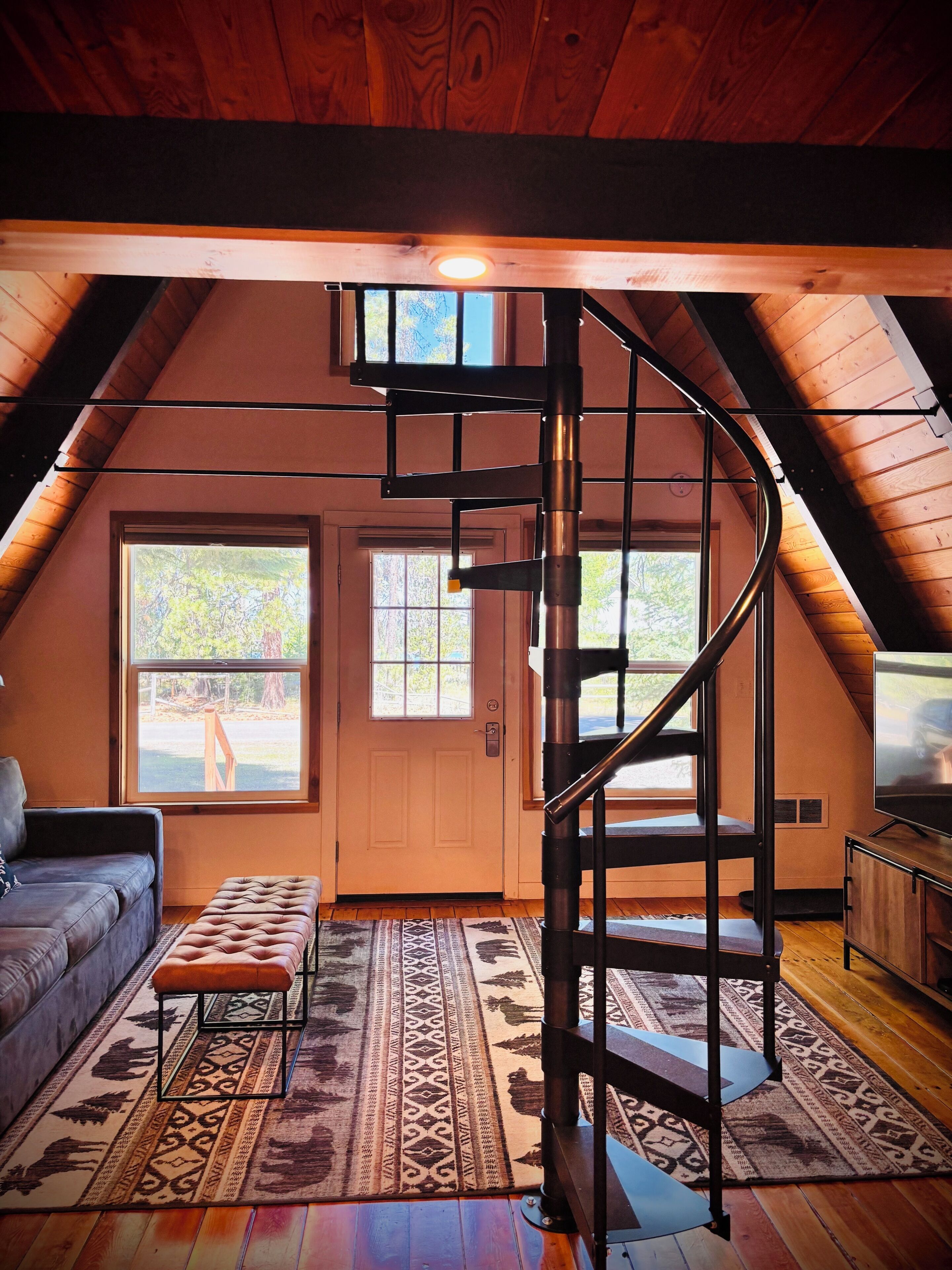 Une pièce de style loft avec un escalier en colimaçon, un canapé, un tapis à motifs et un téléviseur.