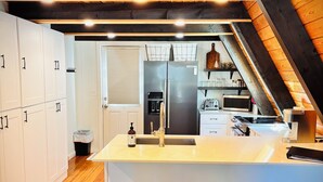 Une cuisine moderne avec des meubles blancs, un réfrigérateur en acier inoxydable et des tabourets en bois.