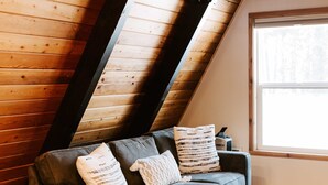 Une pièce de style loft avec un plafond en pente, un canapé gris agrémenté de coussins à motifs, une petite table ronde et un tapis à motifs.