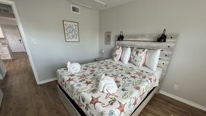 Un dormitorio con cama, cabecera, un letrero en la pared y un pasillo.