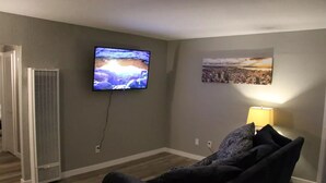Un salon avec un téléviseur à écran plat fixé au mur, un radiateur mobile, un canapé et une lampe.
